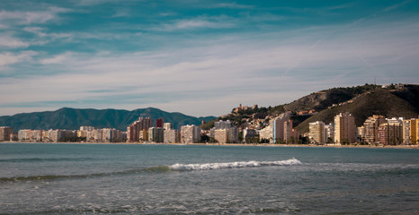 Fototapeta premium Sandy long beach with waves rolling on it on a sunny day by the Mediterranean sea in Valencia, Spain. A shot of tranquil and relaxing vacations in Spain.