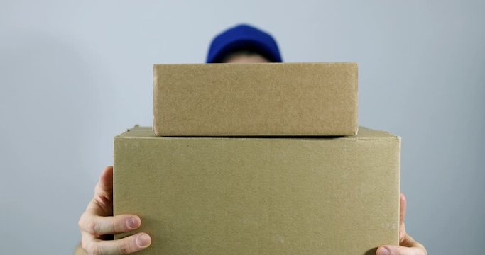 delivery man holding pile of cardboard boxes in front on gray background