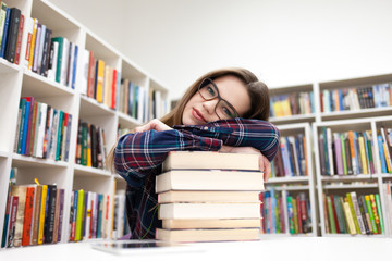 Beautiful student leaned her head on a pile of books. Young woman in library concept