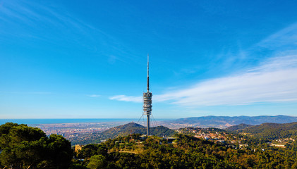 Fototapeta premium Barcelona Spain view from Mount Tibidabo of television tower and city. Scenic panorama with green hills and blue sky.