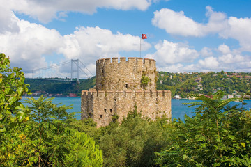 Fototapeta na wymiar The Halil Pasha Tower defensive flag tower in the grounds of the 15th century Rumeli Hisari fort in the Sariyer district of Istanbul, Turkey. The Fatih Sultan Mehmet Koprusu Bridge and the Kavacik are
