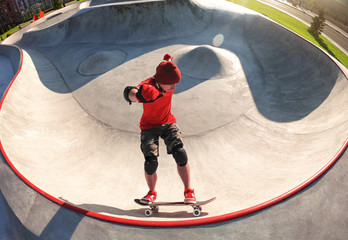 Young active skateboarder riding skateboard in skatepark pool at sunny summer day - obrazy, fototapety, plakaty
