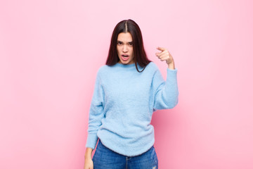 young pretty woman pointing at camera with an angry aggressive expression looking like a furious,...