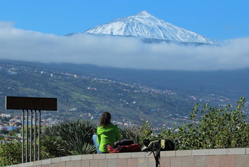 Fototapeta na wymiar Young woman looks from the Mirador de Humbold at the snowy Teide volcano in Tenerife and over the Orotava valley