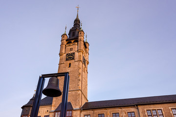 Obraz premium Germany, Saxony-Anhalt, Dessau-Rosslau: Facade of city hall tower in late afternoon sunlight and bell monument (No Violence - Keine Gewalt) in the center of the famous German town - administration