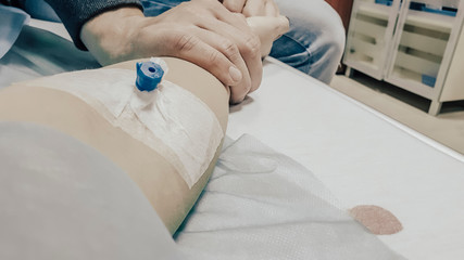 The concept of emotional support. Closeup of a catheter in a female hand. Man holding tightly the hand of a woman, who lying in a hospital bed. Covid-19