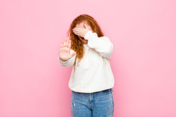 young red head woman covering face with hand and putting other hand up front to stop camera,...