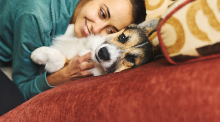 Portrait of young smiling woman hugging pet. Cute Welsh Corgi puppy resting with owner, spending time together at home. Concept friendship with dog and human, cute moments, relaxing, carefree. focus