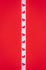 Minimalistic valentine's day or wedding composition with white ribbon with small hearts on a red paper background, flat lay, top view, copy space