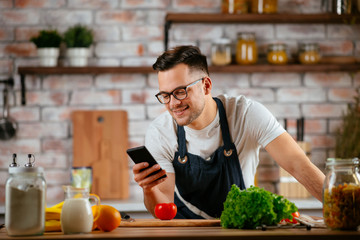 Young man in kitchen. Chef using phone while making food. 