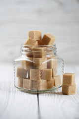 Brown sugar cubes in glass jar on light background