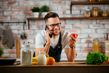 Young man in kitchen. Chef using phone while making food. 