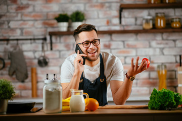 Fototapeta na wymiar Young man in kitchen. Chef using phone while making food. 