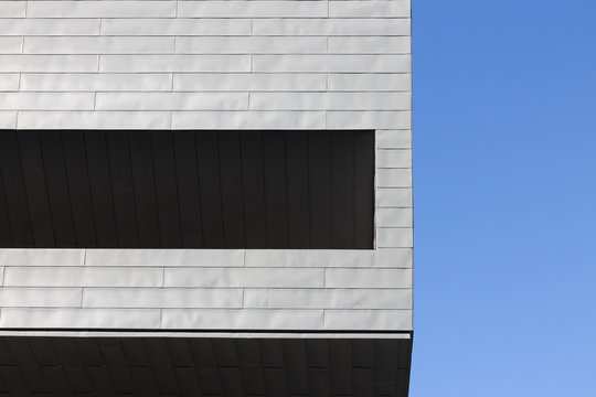 Fachada edificio modernista con baldosas grandes de color blanco con balc&oacute;n interior oscurecido y cielo totalmente despejado.
