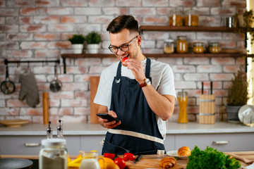 Young man in kitchen. Chef using phone while making food. 