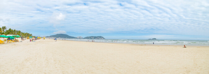 Panoramic view of the Enseada beach - Praia da Enseada - Guaruja SP Brazil. People on the beach, sunshades on the sand and the sea. Brazilian tourist destination.