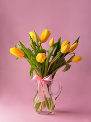Bouquet of yellow tulips in a glass vase on a pink background.