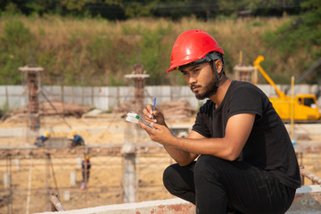 Black bearded engineer wear red hard hat and black working suit make decision in construction site