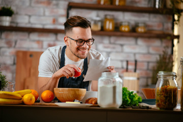 Portrait of handsome man in kitchen. Young man cooking while reading recipe. 