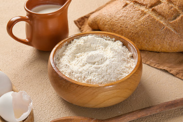 Bowl with flour, milk and bread on table