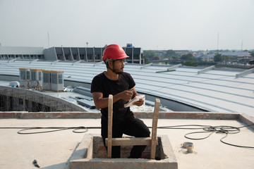 Black bearded engineer wear red hard hat and black working suit climbing wood ladder in construction site