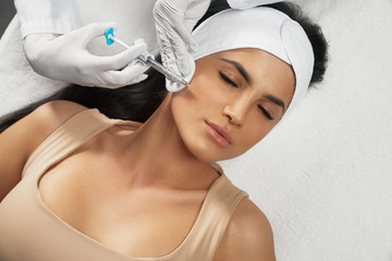 Cosmetologist using syringe to correct female face.