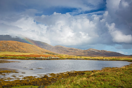 Tranquil view clouds rainbow over rolling hills beyond lake, Loch Aineort, South Uist, Outer Hebrides