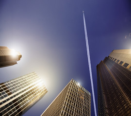 Airplane vapor trail in blue sky above highrise buildings, travel concept