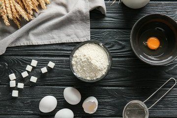 Bowl with flour, eggs and sugar on dark table