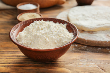 Bowl with flour on wooden table