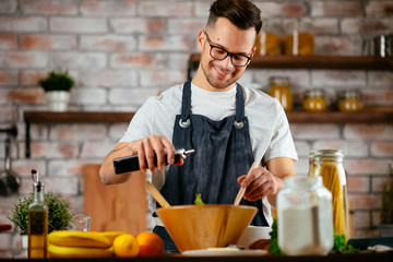 Young man making meal. Chef preparing salad in modern kitchen