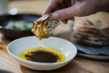 Close up hand dipping bread in olive oil and balsamic vinegar