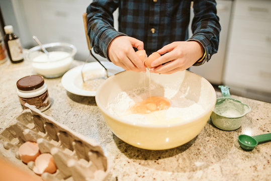 Boy Baking, Cracking Egg Into Bowl In Kitchen