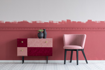 Stylish small pastel pink chair next to trendy pink and burgundy commode