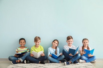 Cute little children reading books on color background