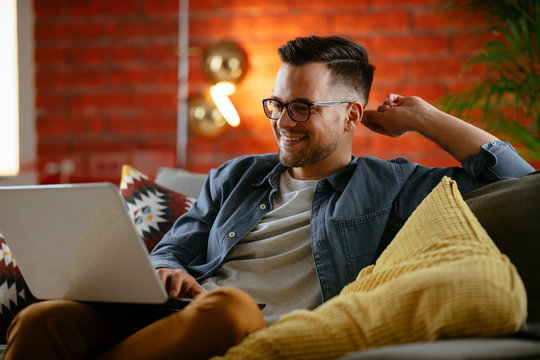 Young man working from home. Businessman sitting on sofa and using laptop. 