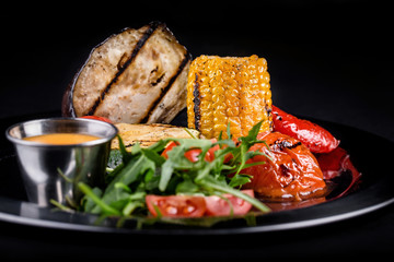  black plate with grilled vegetables eggplant tomatoes cabbage peppers and corn with sauce