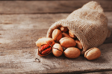 Pecans are spilled out of a burlap bag onto a wooden table in close-up. - Powered by Adobe