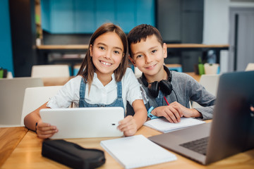 Two happy small friends writing homework , using smart digital tablet at modern blue classroom.