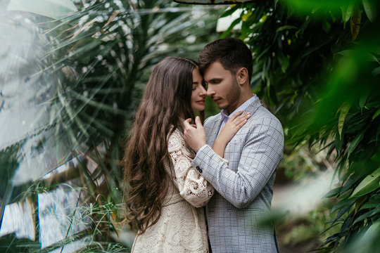 Romantic couple, bride and groom posing in a greenhouse against the background of plants in the garden. Advertising space