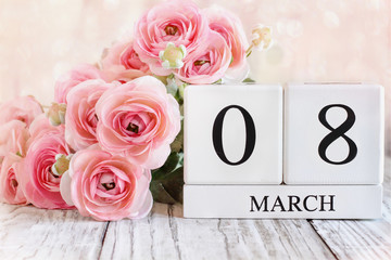 White wood calendar blocks with the date March 08 for International Women's Day and pink ranunculus flowers over a wooden table.