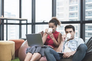 couple using laptop, holding a cup and smiling while sitting on beanbag chairs
