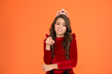 Not you. Kid wear golden crown symbol of princess. Girl cute baby wear crown stand orange background. Childhood concept. Girl dreaming to become princess. Lady little princess. Pointing at camera