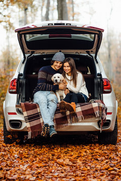 Young couple have a picnic time with their small labrador in automobile in the autumn forest.