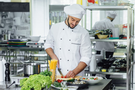 Chef cooking with knife vegetables. Young bearded man at his work place, food concept. Lifestyle.