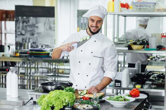 Young, bearded and successful smiling male, specialist, cook chef staywith knife in modern kitchen.