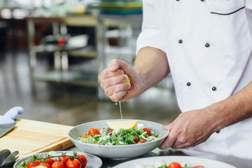 Man, cook chief squeezes lemon for spaghetti carbonara, with sharp knife and cooking vegetables salad in kitchen.