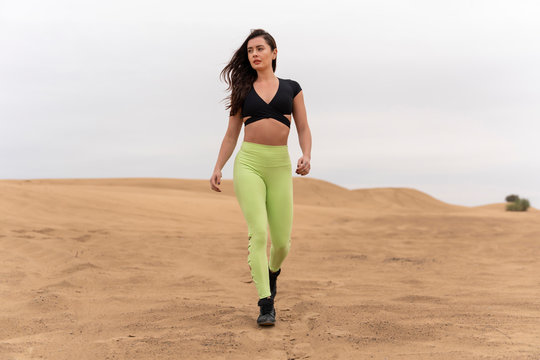 Beautiful latin brunette fitness model wearing lime green long tights and black top walking strong in the Middle Eastern Desert