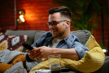 Young man listening music. Attractive man sitting on sofa and listening music in living room.