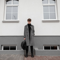 Attractive young man in a long plaid fashionable coat in black stylish boots with a cool leather...